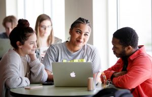 Students talk together while sitting around a laptop