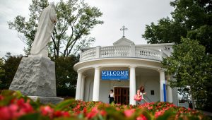 Students walk by the Marymount chapel where there's a Welcome Saints sign. The Ave Maria statue rests on the side of the image.