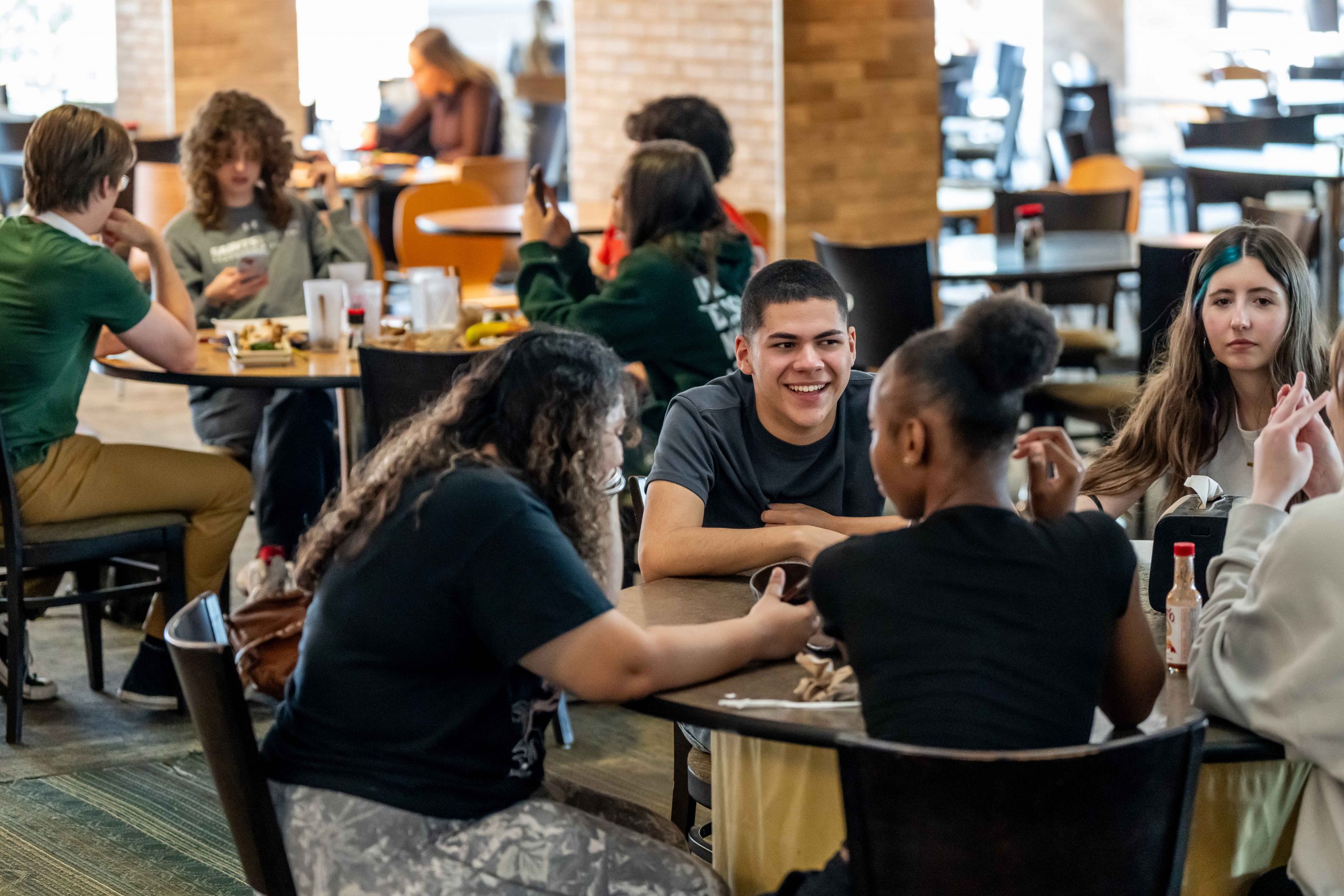 Students sit at a cafeteria table and smile