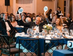 A group of men and women, including Marymount President Irma Becerra, sit at a table and raise auction numbers for the Halo Awards.