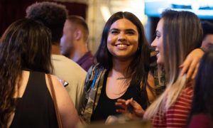 A young alumna smiles through a crowd of other young alumni.