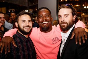 Three young alumni smile with their arms around each others' shoulders during an alumni meetup.