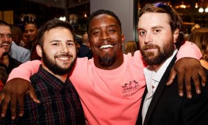 Three men smile with their arms around each others' shoulders