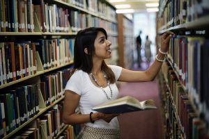 Female student pulls a book off a library shelf.