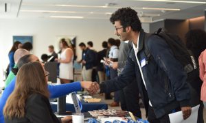 A student shakes hands with people at a career fair booth.
