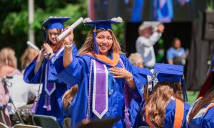 A Marymount graduate waves her diploma while she walks in cap and gown.
