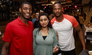 Two men and a woman pose together and smile while in a crowded restaurant
