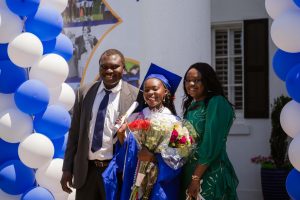 A young alumnae in cap and gown poses with her family.