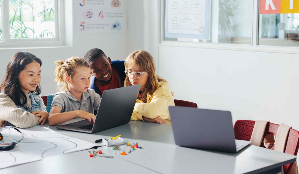 A group of young students huddle around a laptop.