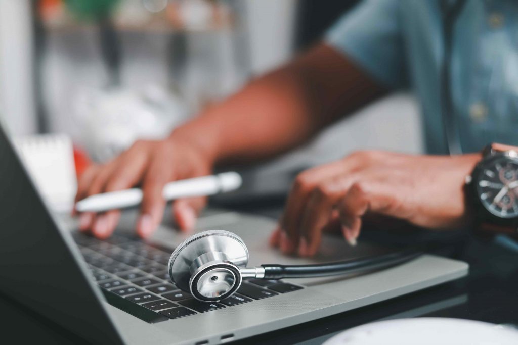 Person typing on a commuter. A stethoscope sits on the side.