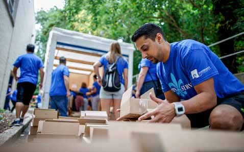 A man in a Marymout Saints Service t shirt organizes boxes while other people unload boxes from a truck