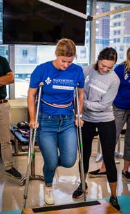 Two girls wear Marymount t-shirts. One is on crutches and the other is helping her.