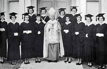 Bishop Ireton stands besides 12 members of the first graduating class who are clothed in cap and gown