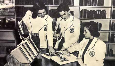 Students from the 1950s point and look together in a textbook. They wear blazers with what look like Marymount's crest.