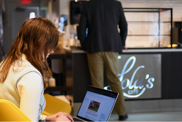 A woman works on her laptop while a man stands at the counter to order.