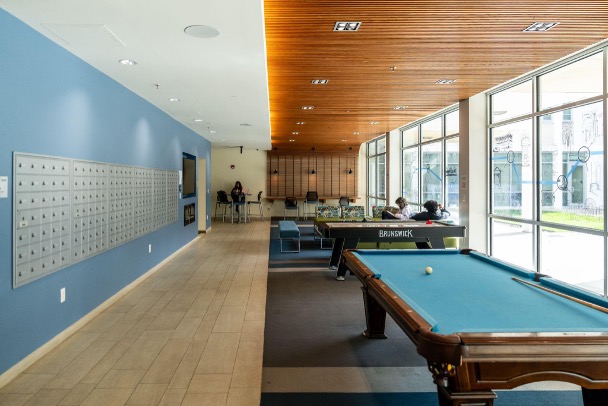 A big room with a pool table, air hockey table, mailboxes, and students hanging out.