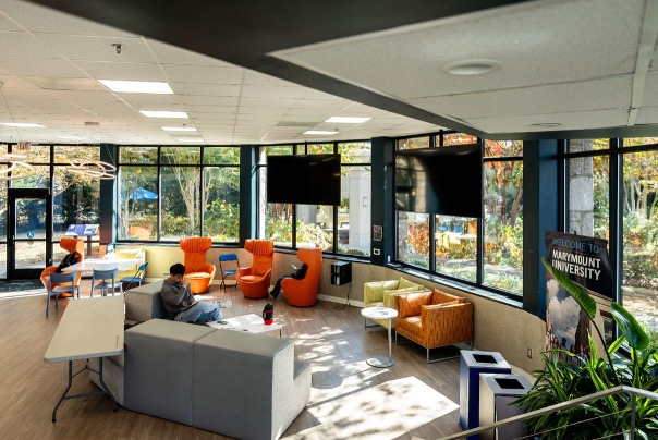 A big room with couches and orange swivel chairs, with tv screens and large windows
