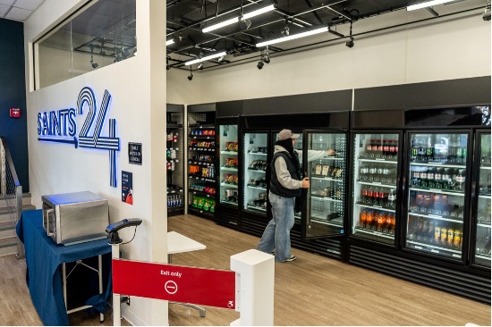 A wall of refrigerators lines the side of the room. A student pulls a soft drink out of one.