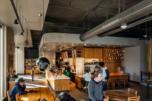 People sit at tables in a cozy, industrial cafe with wooden tables and counters.